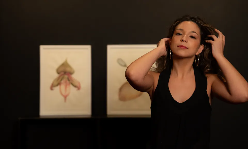 Amanda está em primeiro plano com três de suas obras ao fundo.